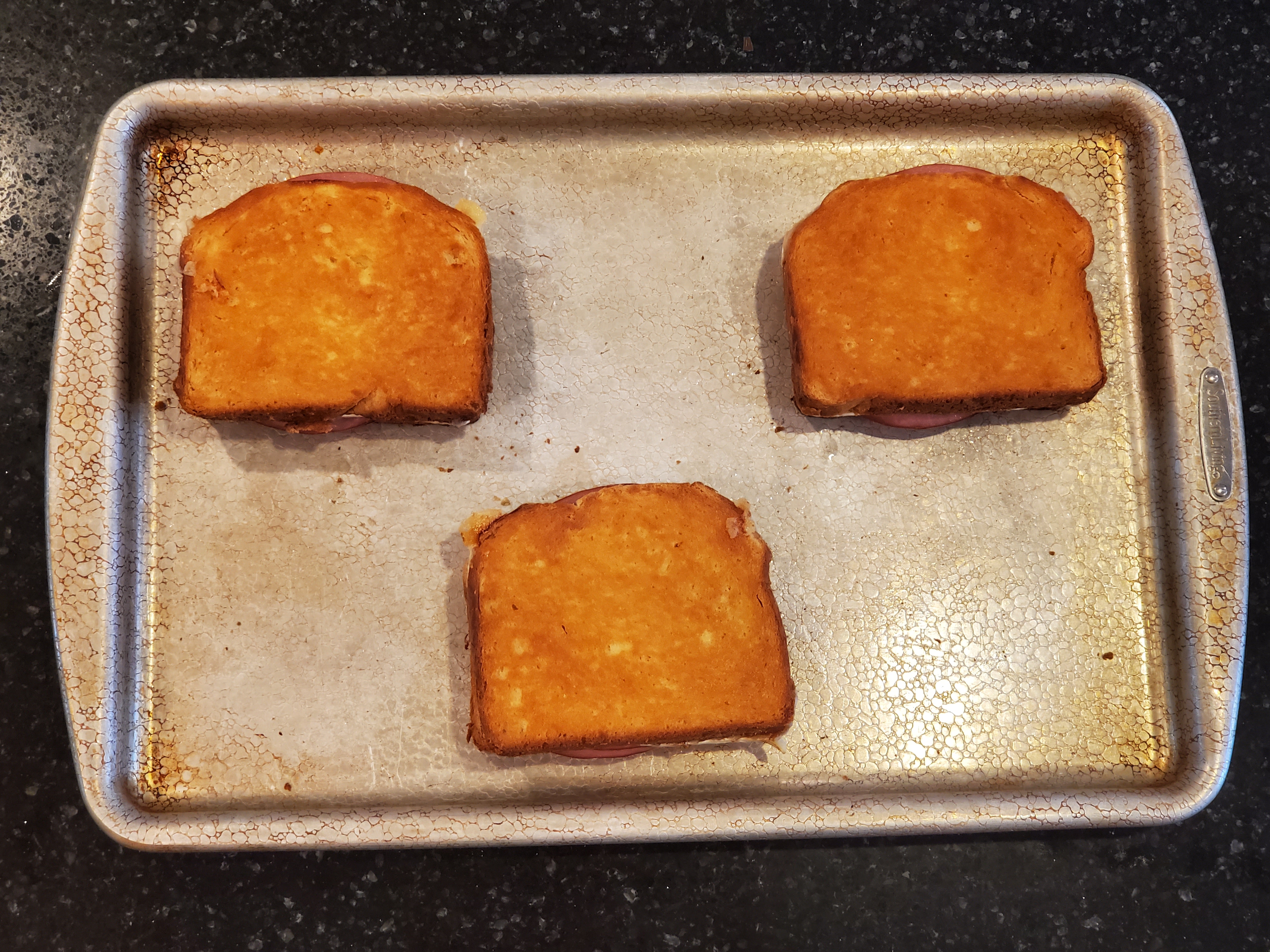 The three sandwiches have come out of the oven, golden brown and sit on the baking sheet.