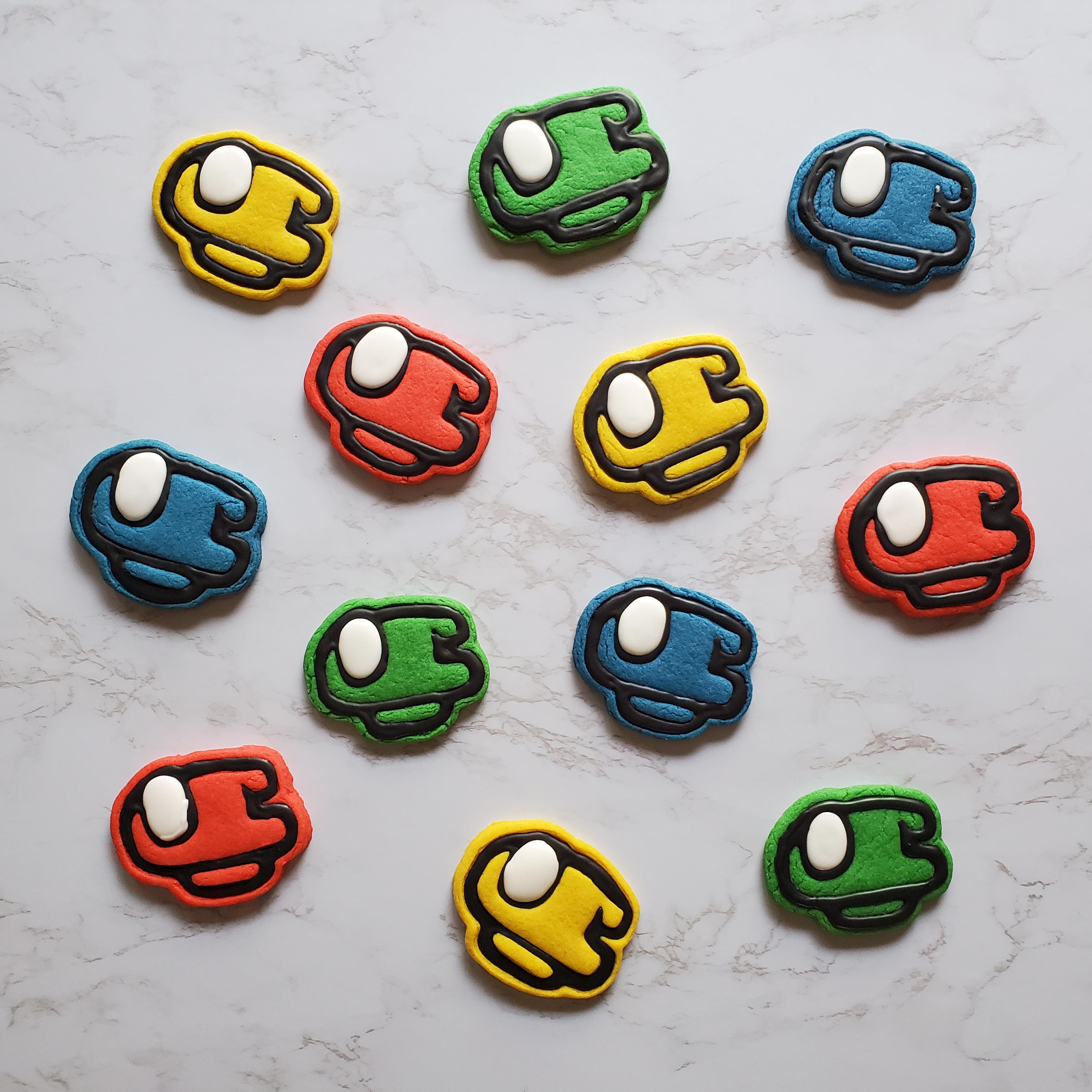 Among us cookies in the colors red, yellow, green and blue, laying on a marble countertop.