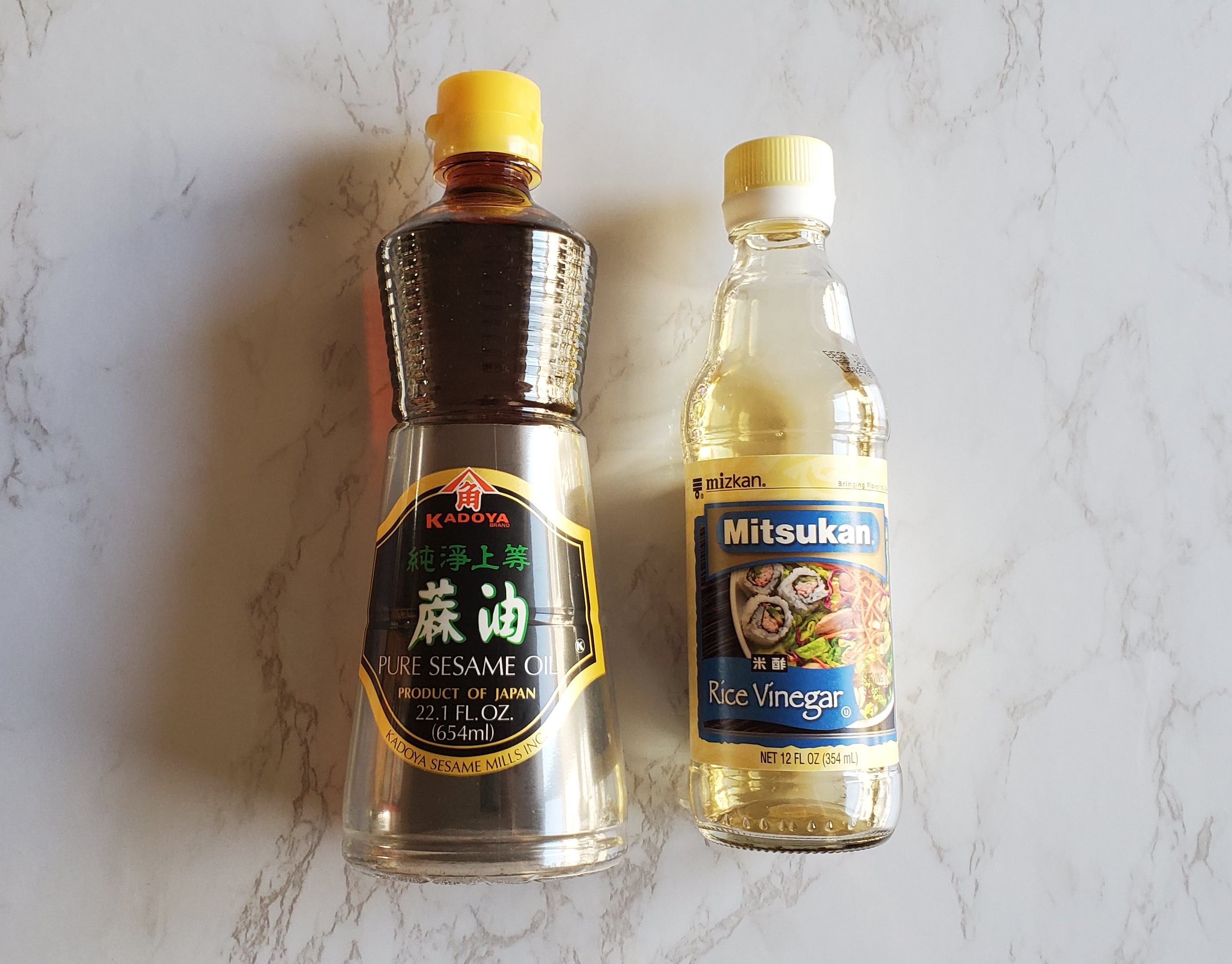 Sesame oil and rice vinegar on a white marble background.