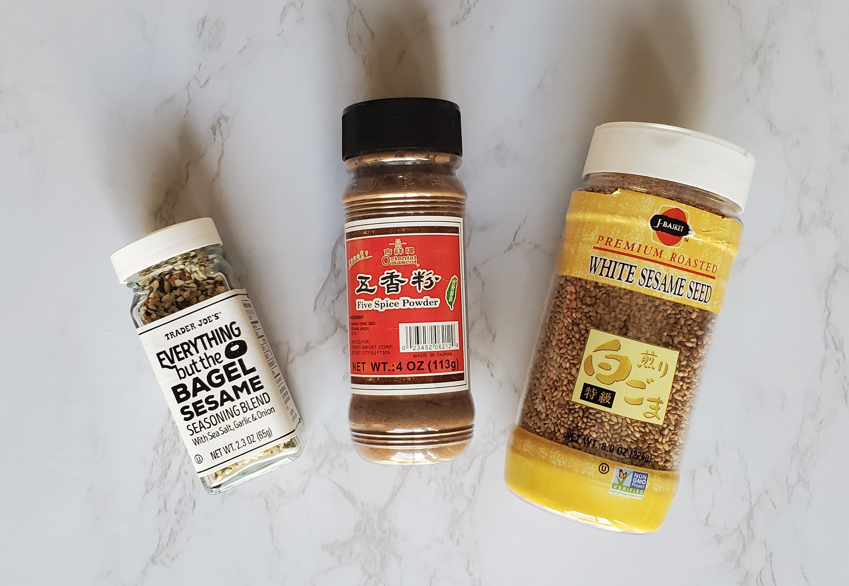 From left to right, a small jar of Trader Joe's Everything But the Bagel Seasoning, a jar or Chinese Five Spice and a large jar of white sesame seeds.
