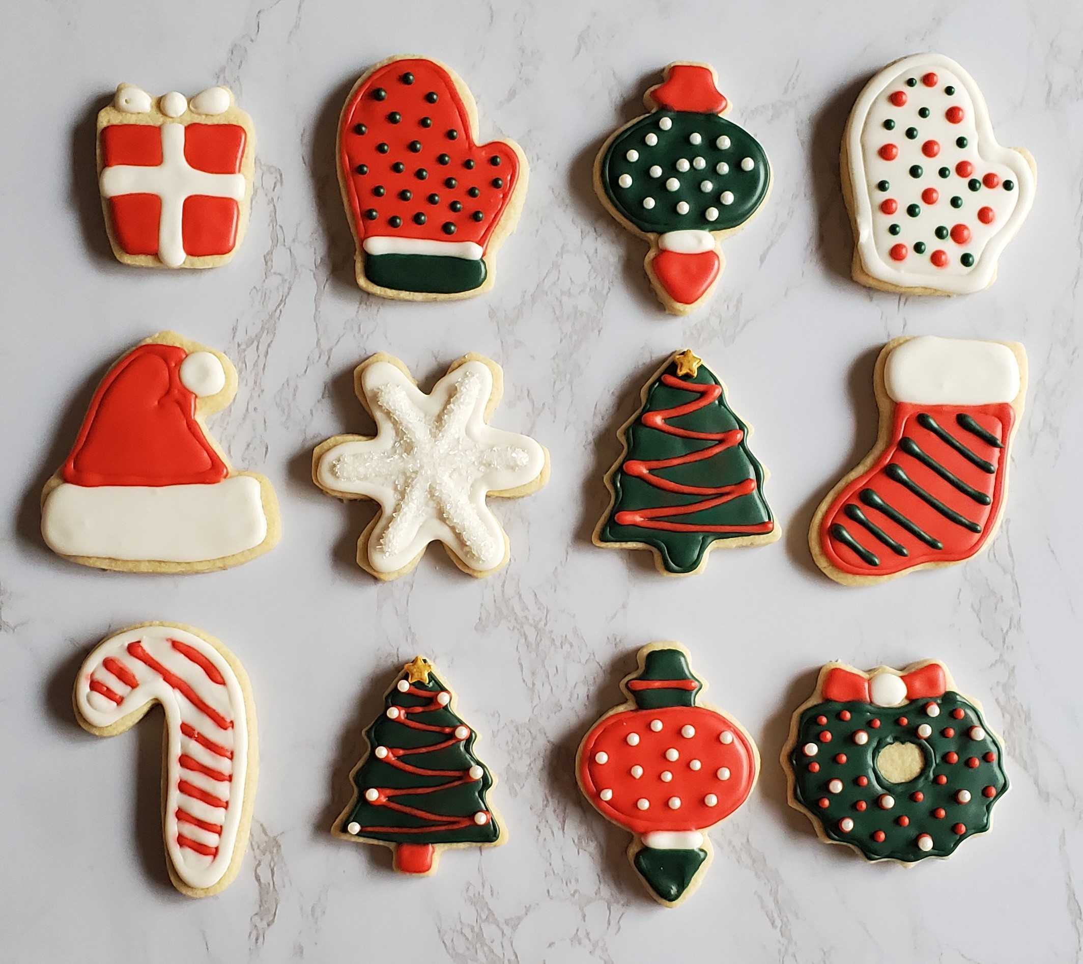 Christmas cookies in the shapes and decorated as gifts, mittens, ornaments, snowflakes, candy canes, christmas trees, wreaths and stockings. Decorated with royal icing in red white and green and sprinkles!
