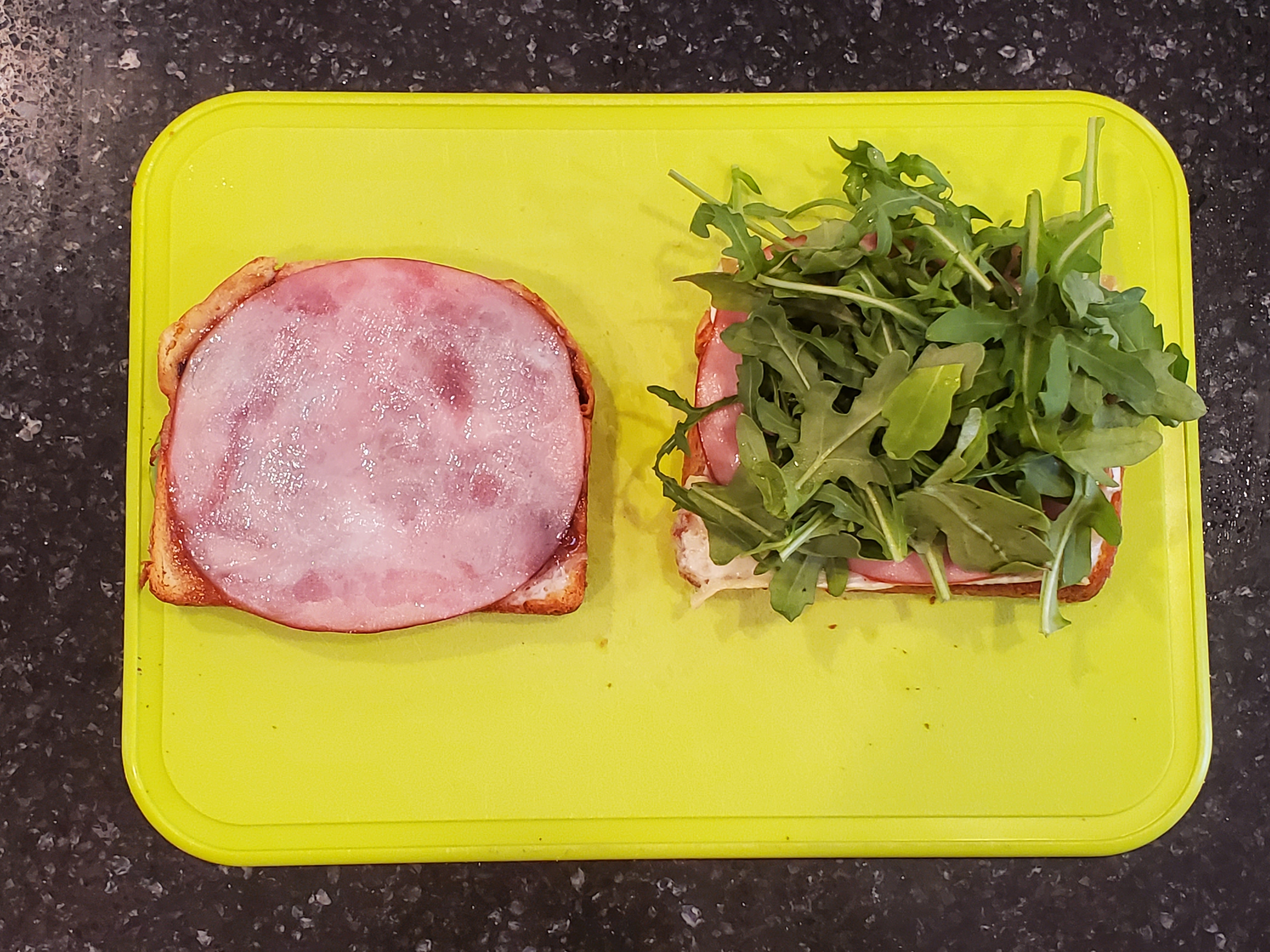One of the sandwiches sits open-faced on a bright lime green cutting board with a handful of arugula on the right half.