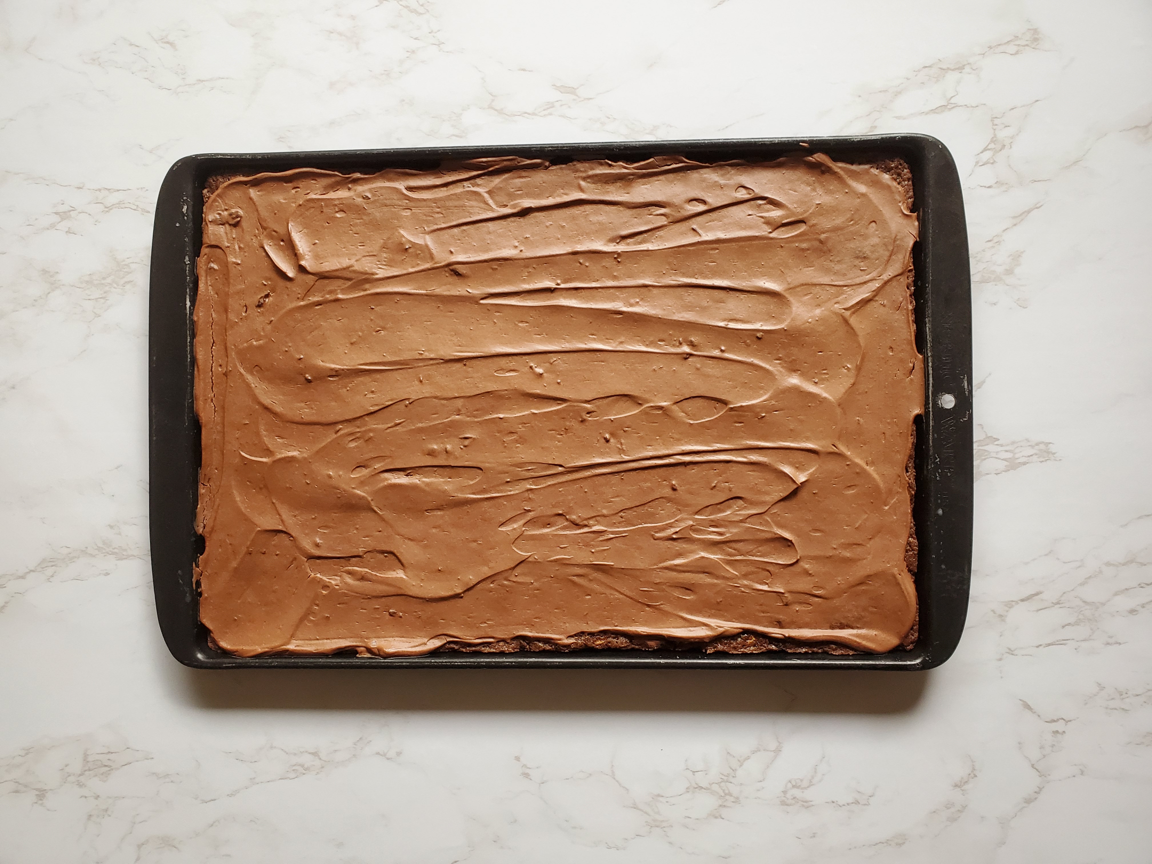 A baking sheet of vegan zucchini brownies on a white marble counter.