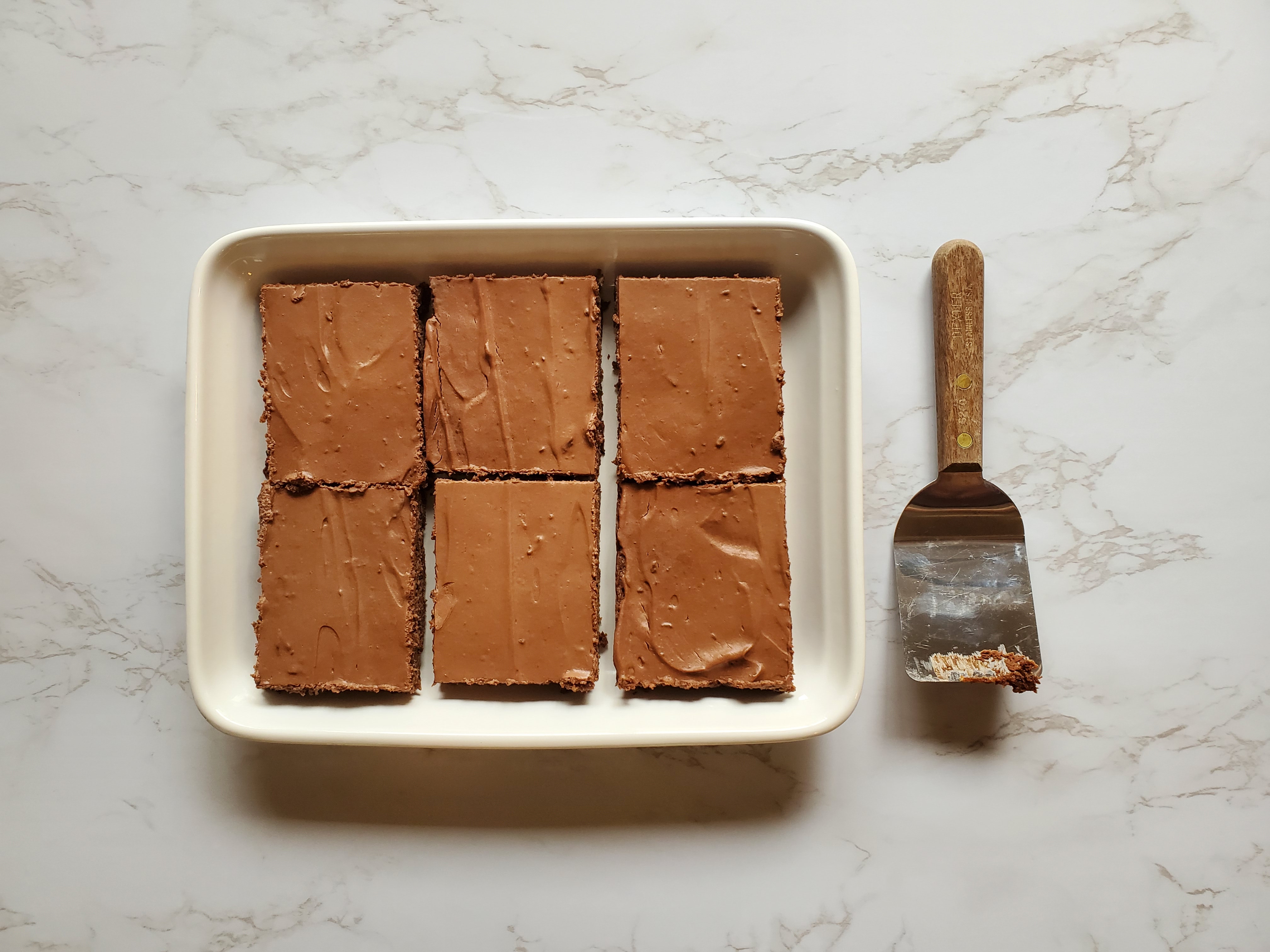 Vegan brownies, cut in squares, on a white tray with a server, on a white marble counter top.