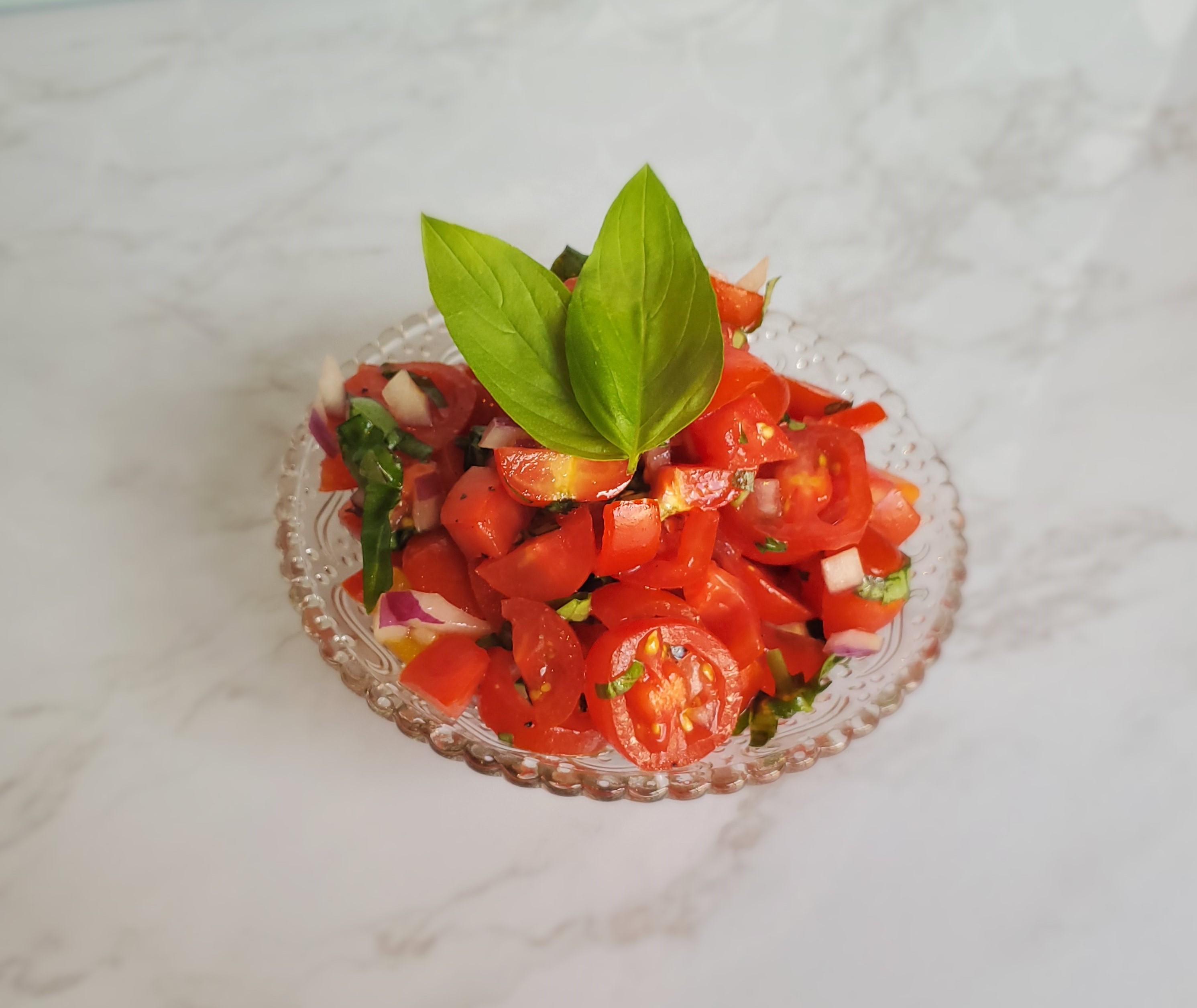 Bruschetta in a vintage glass bowl on top of a marble countertop.