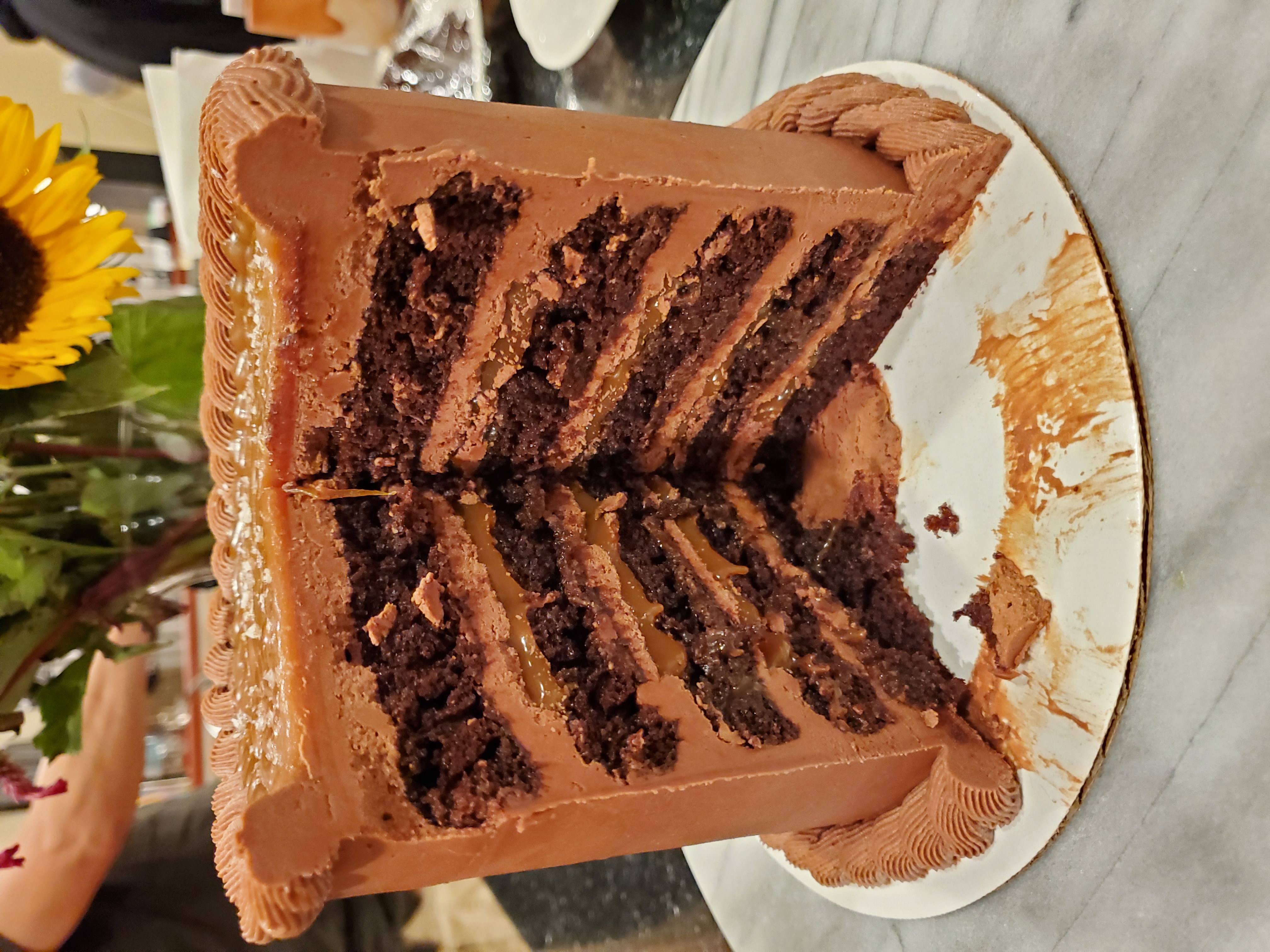 A five layer chocolate cake with gooey caramel in between each layer on a grey granite turn table on a black granite coutertop.