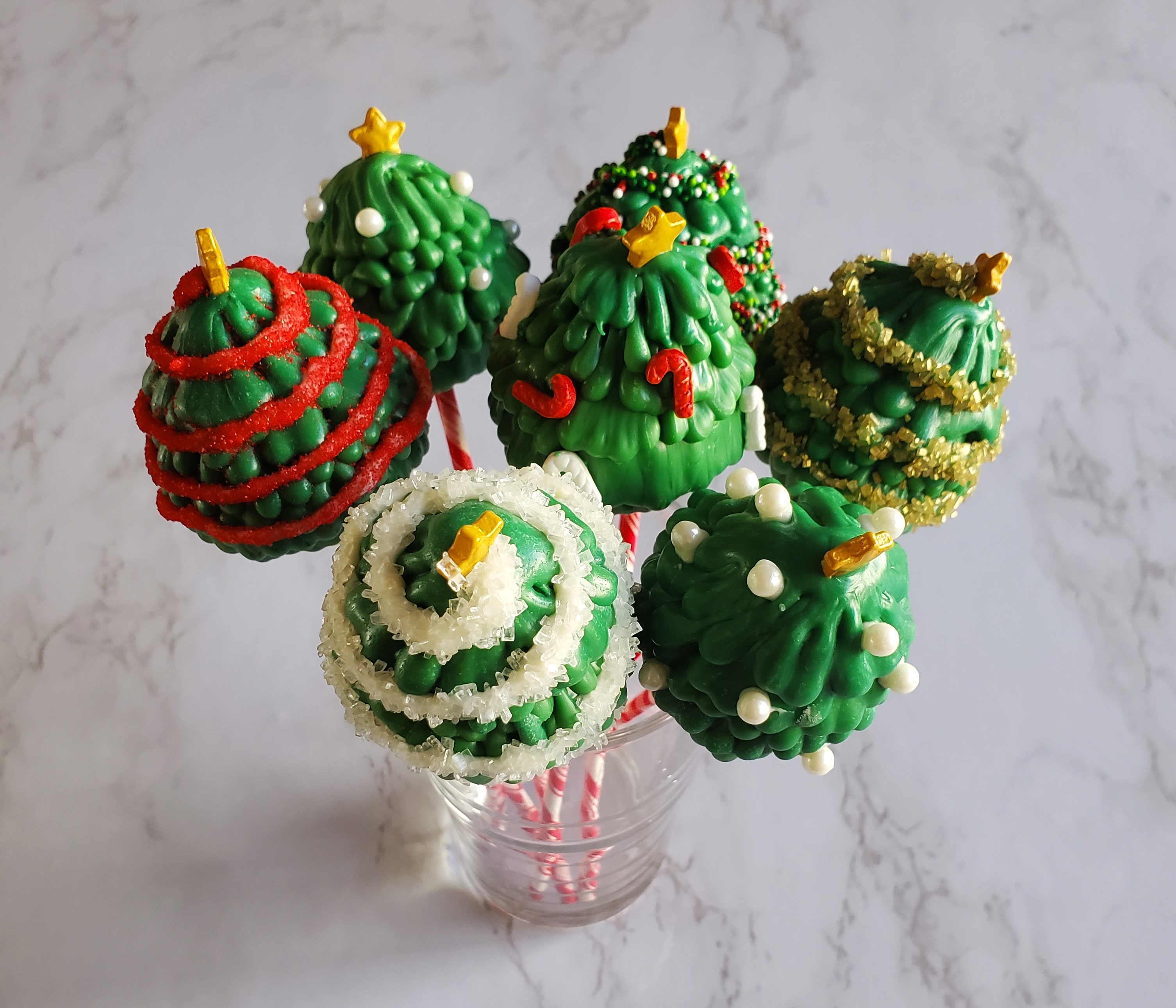 Christmas tree cake pops in a cup on a white marble background.