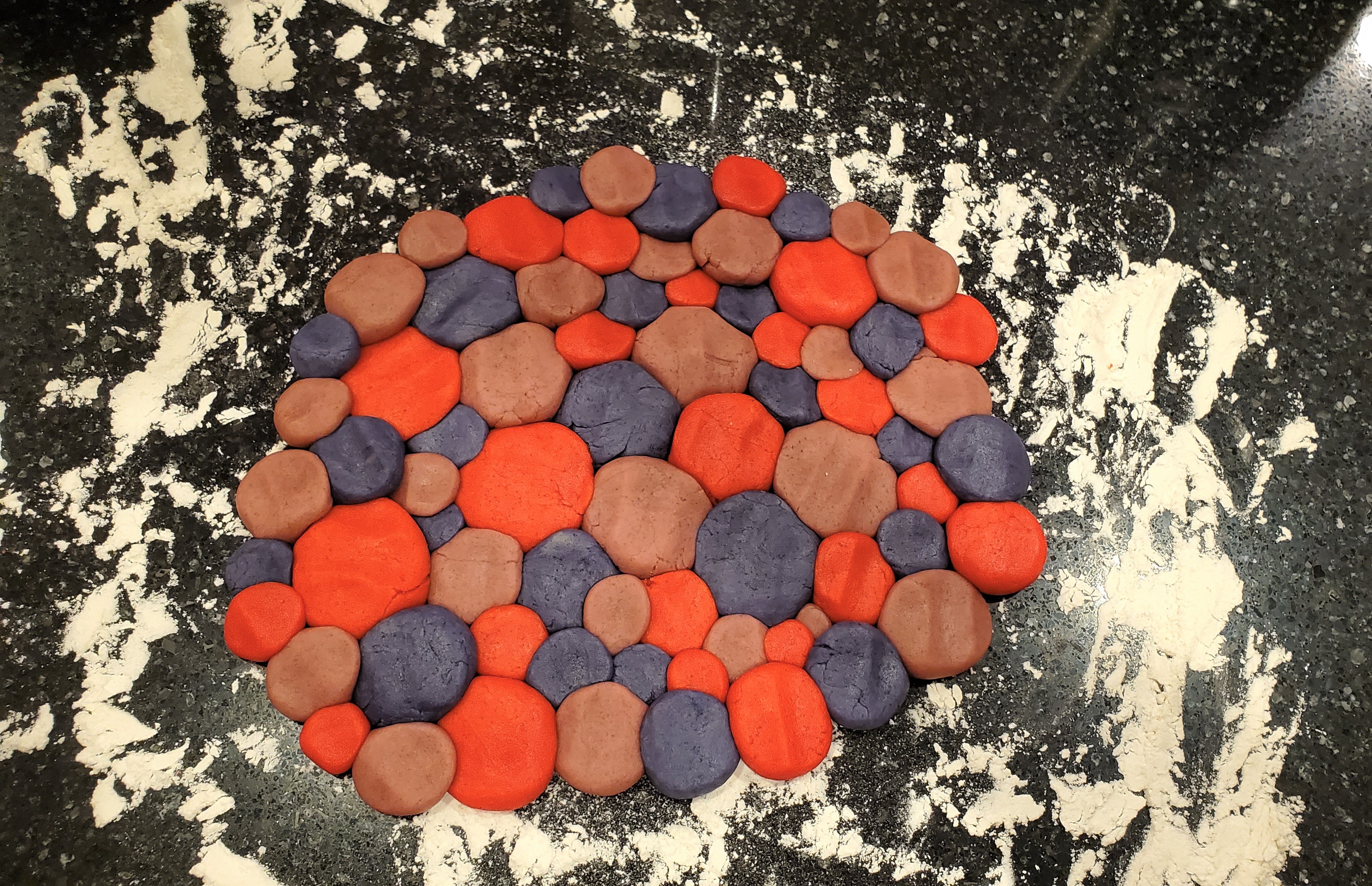 Little balls of dough all pressed together on a black countertop with flour.