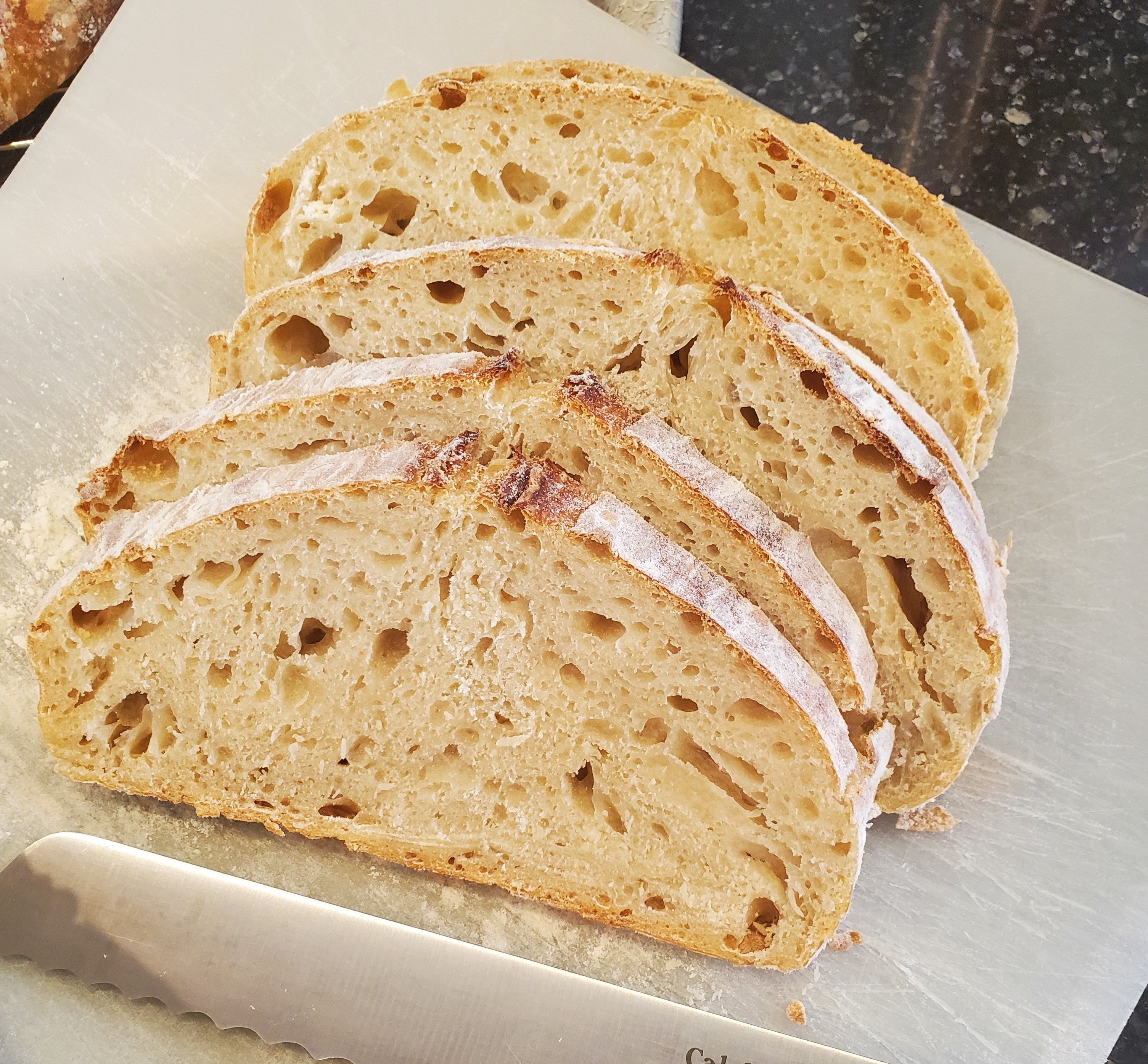 Four slices of airy sourdough displayed on a white plastic cutting board with a serrated knife sitting in front.