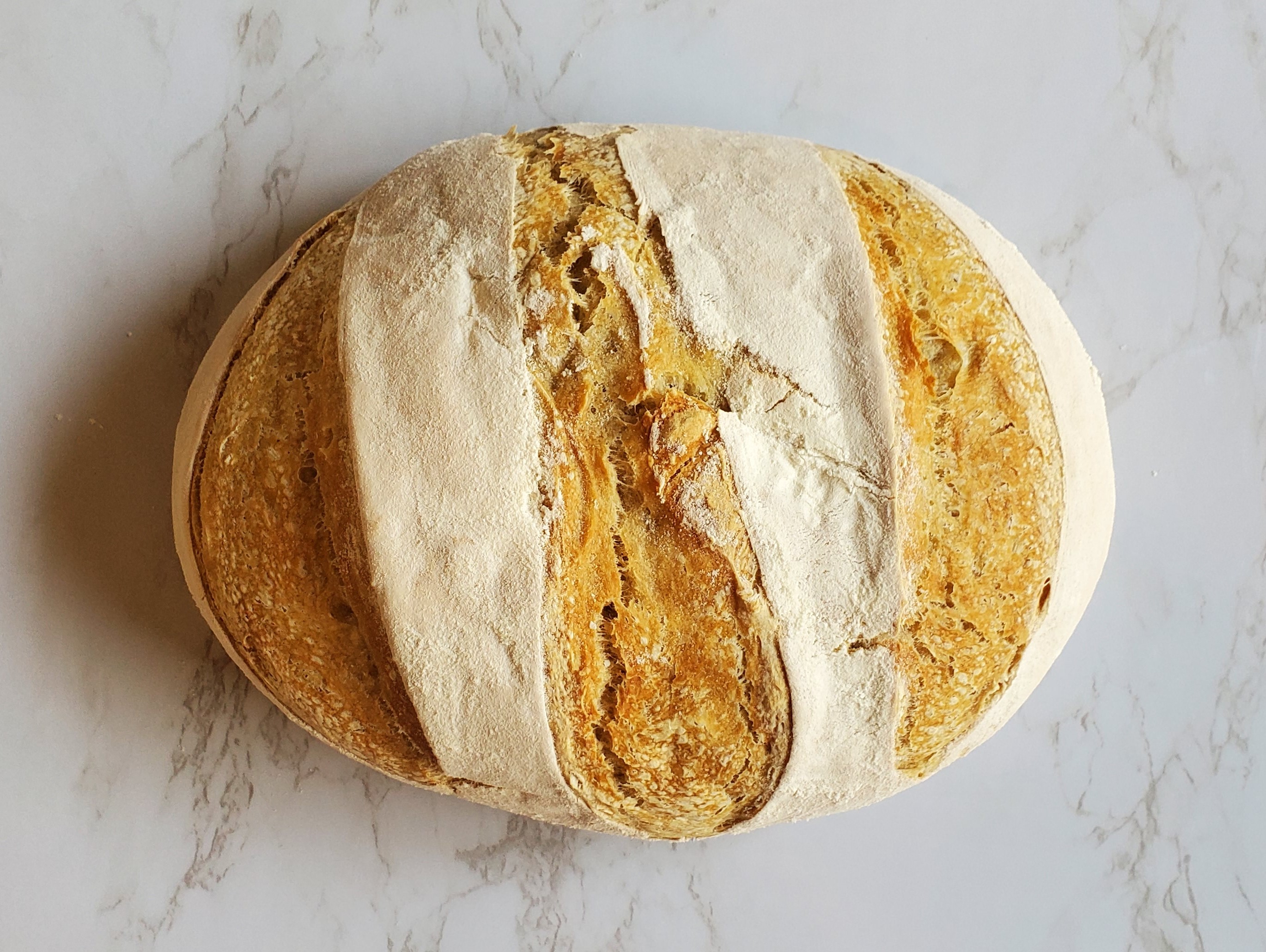 A crusty, full sourdough loaf sits on a granite marble countertop.