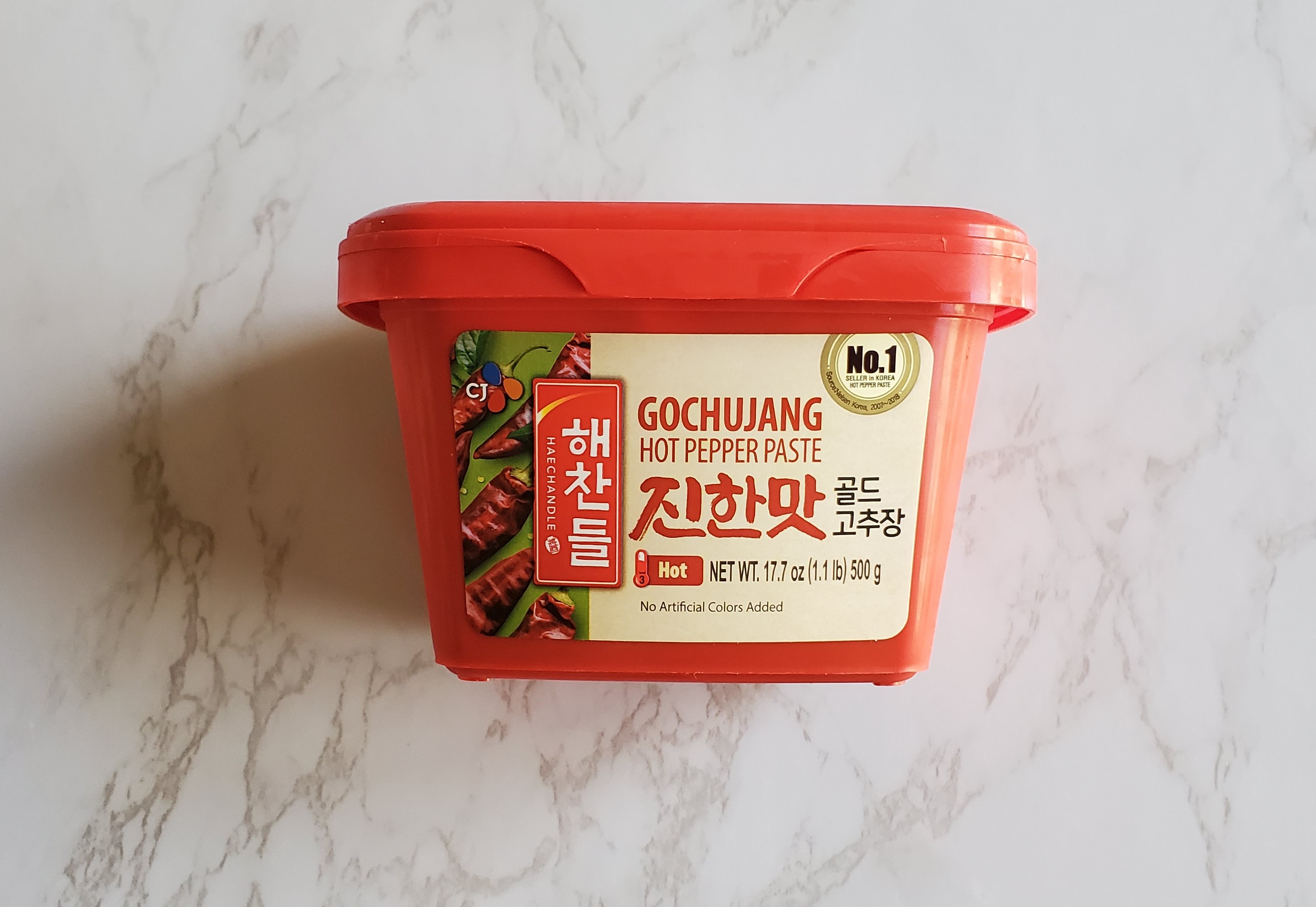 A rectangular container of Korean Gochujang paste sits on a white marble background.
