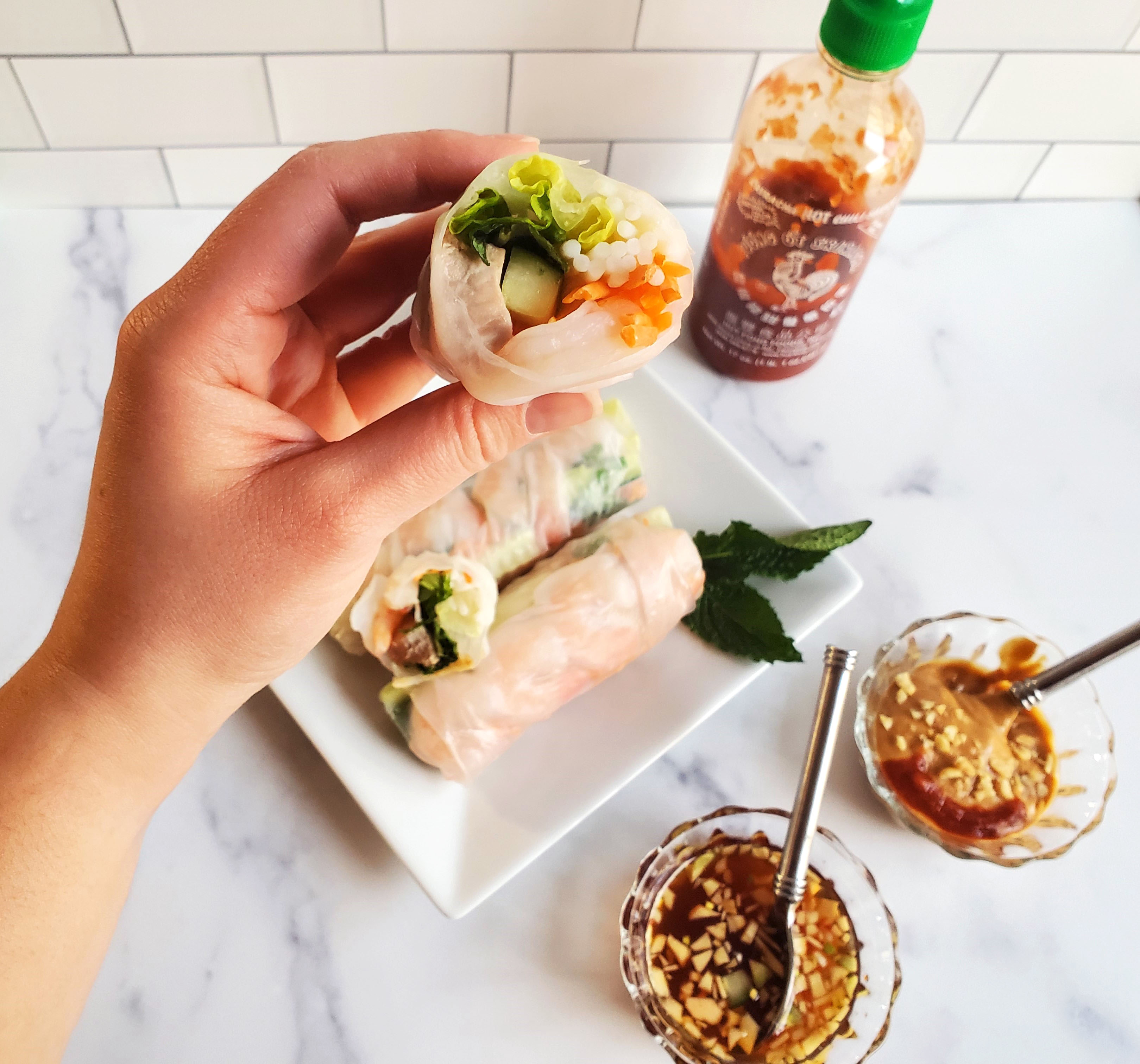 A hand holding a spring roll with a bite out of it, sauces in the background.