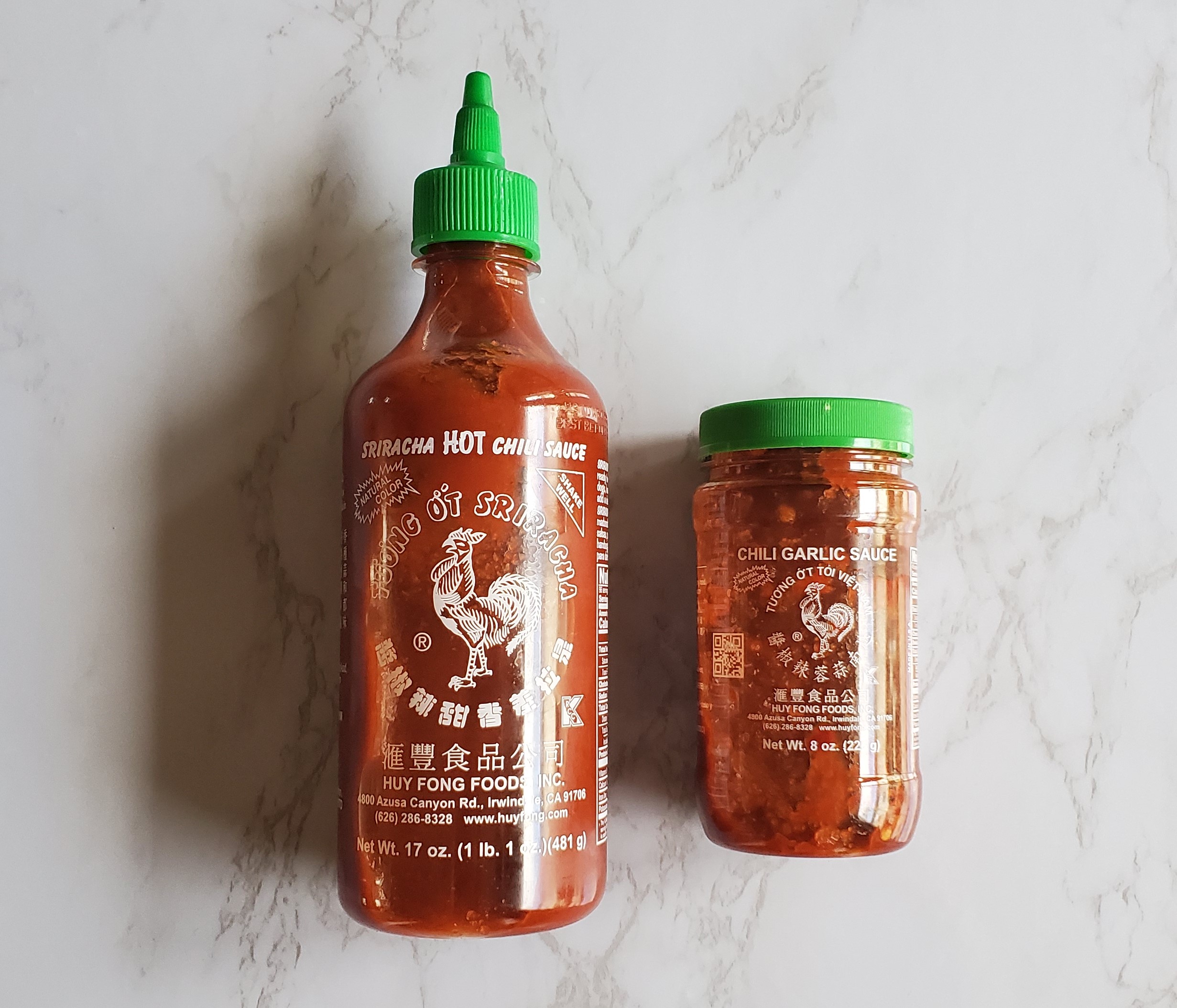 Sriracha and Chili Garlic Sauce on a white marble background.