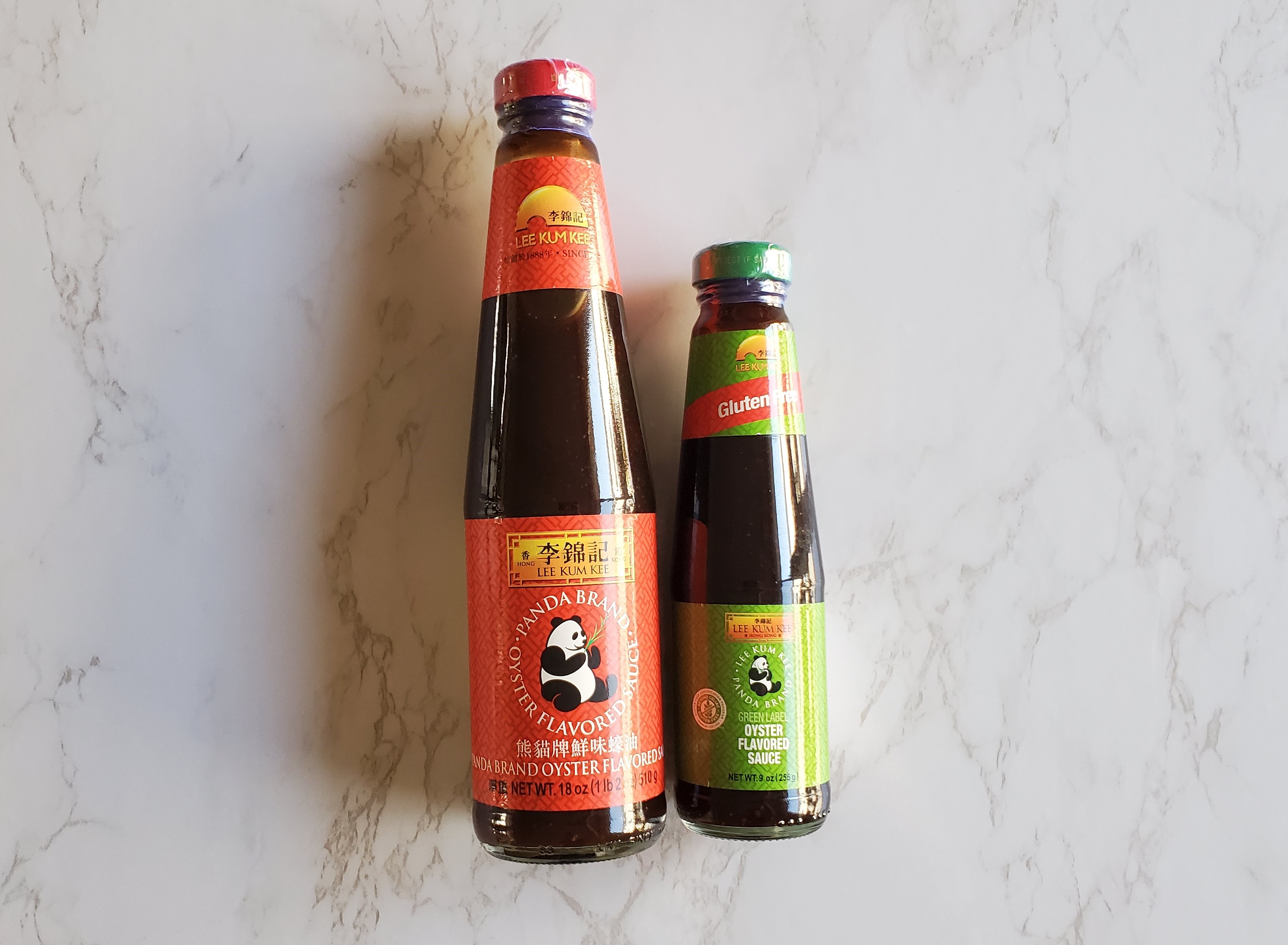 Two bottles of oyster sauce on a white marble background.