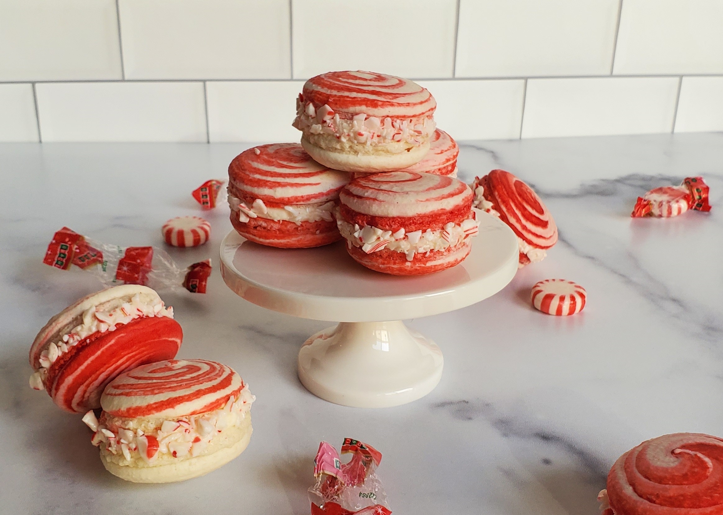 Peppermint swirl macarons on a small pedestal, surrounded by more macarons and peppermints with wrappers.