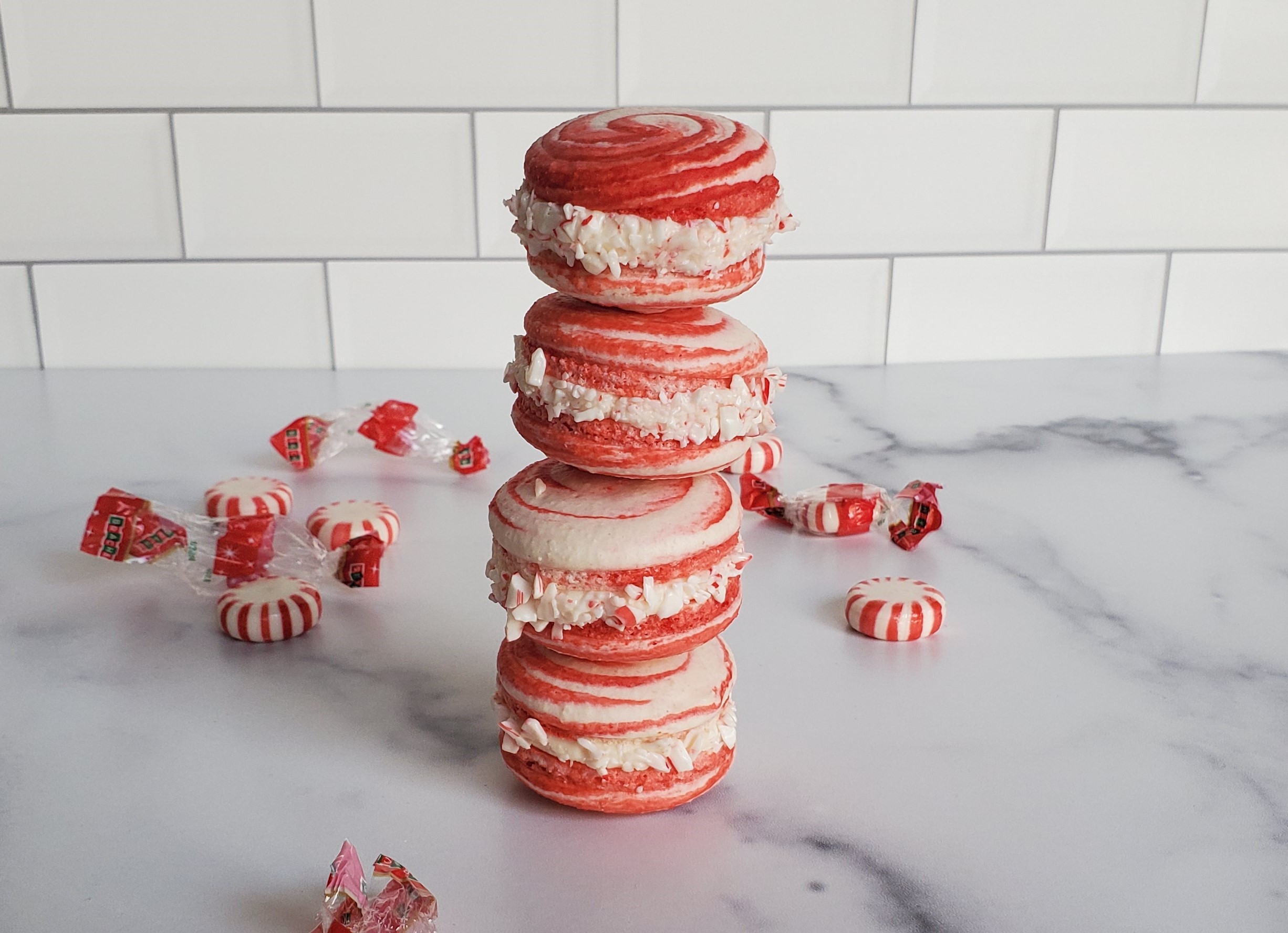 A peppermint macaron tower of 4, surrounded by peppermints and their wrappers.