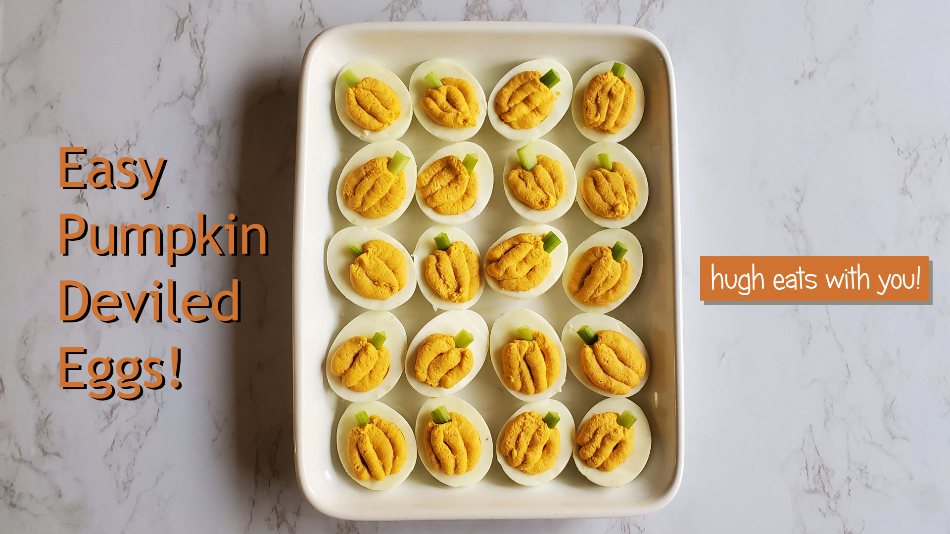 A white rectangular platter on a marble countertop, filled with deviled eggs resembling pumpkins.