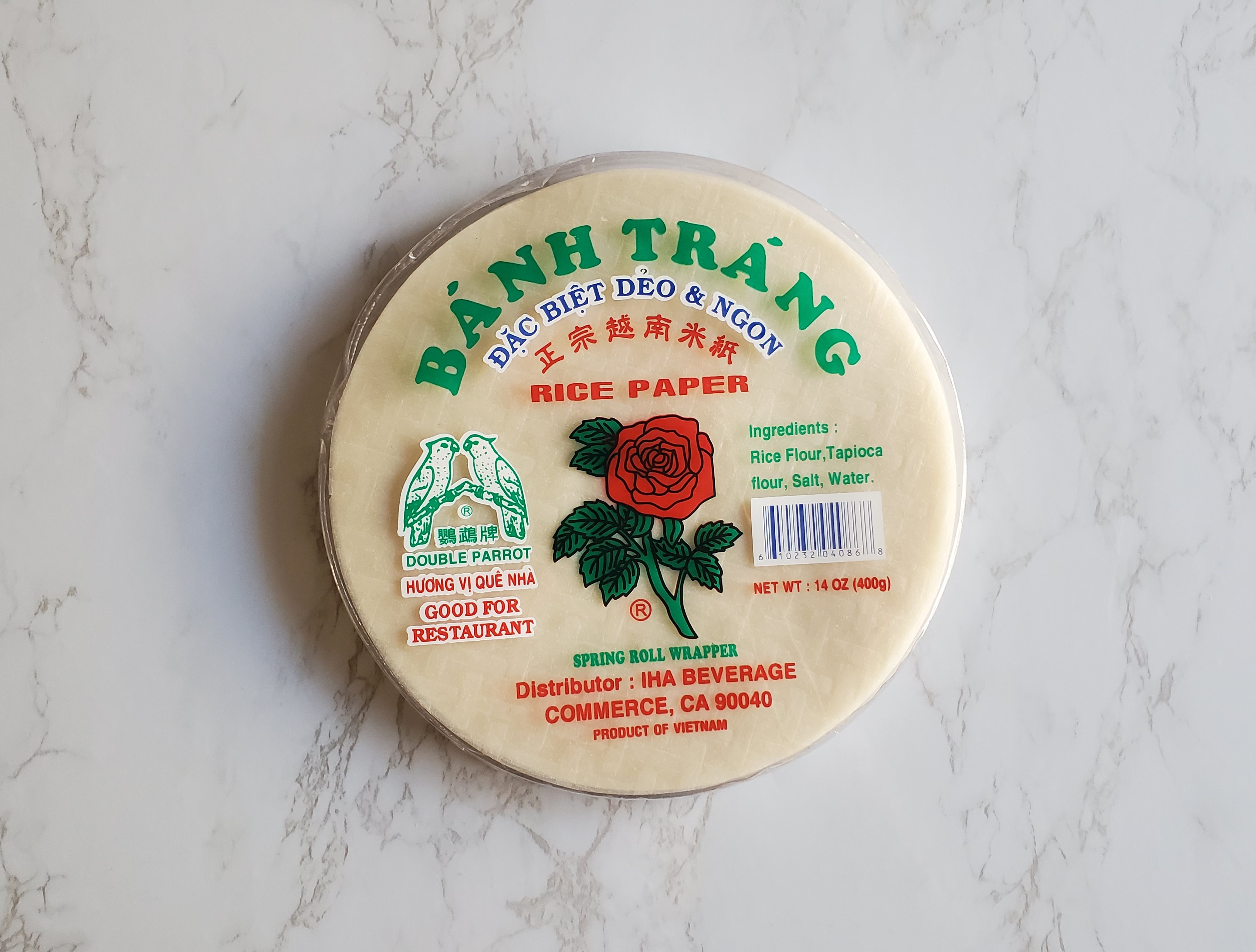 A round container of Banh Trang Rice Paper wrappers sits on a white marble background.