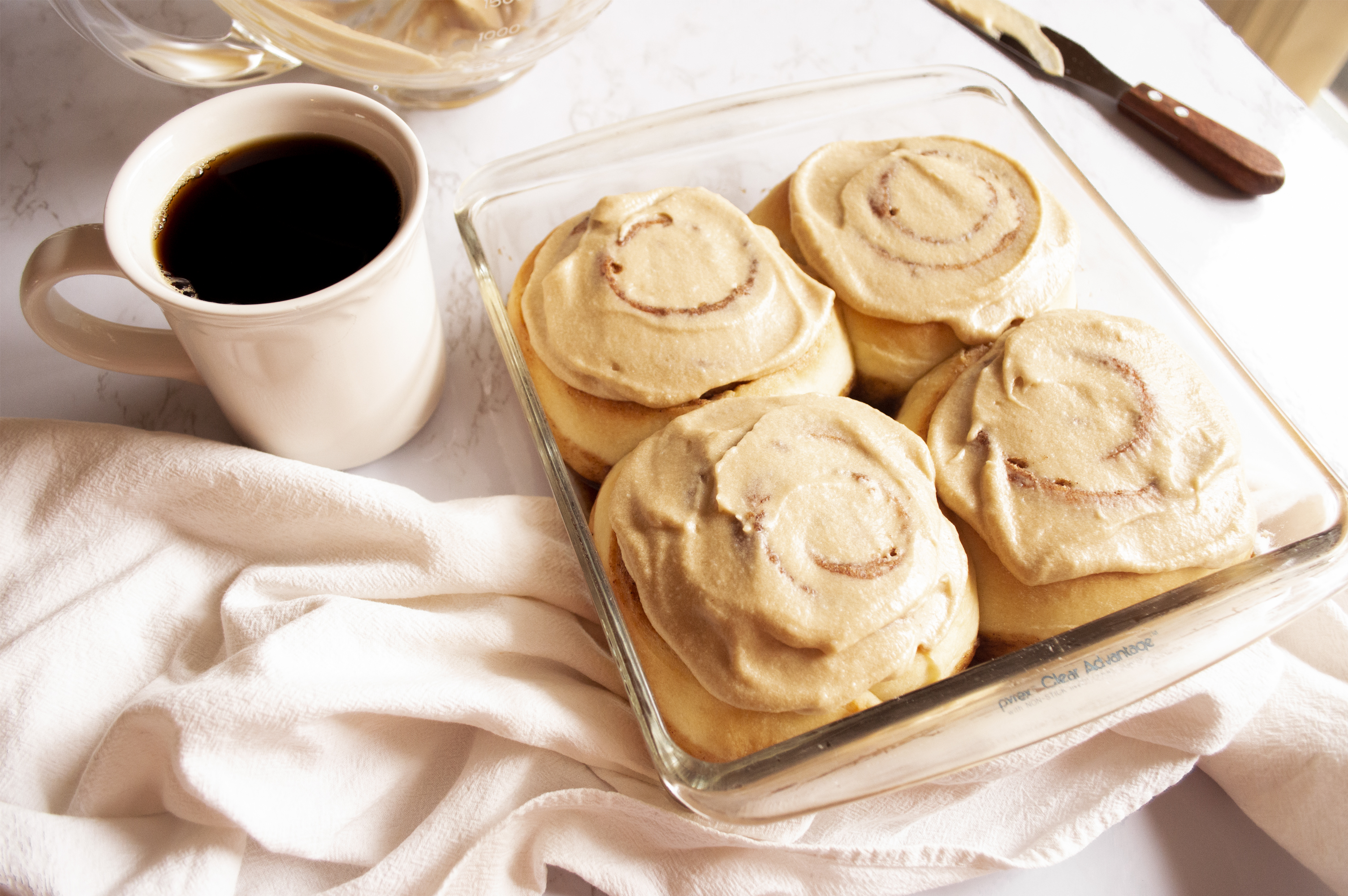 Espresso Cinnamon rolls in a glass pan, a cup of coffee sits on the left hand side.