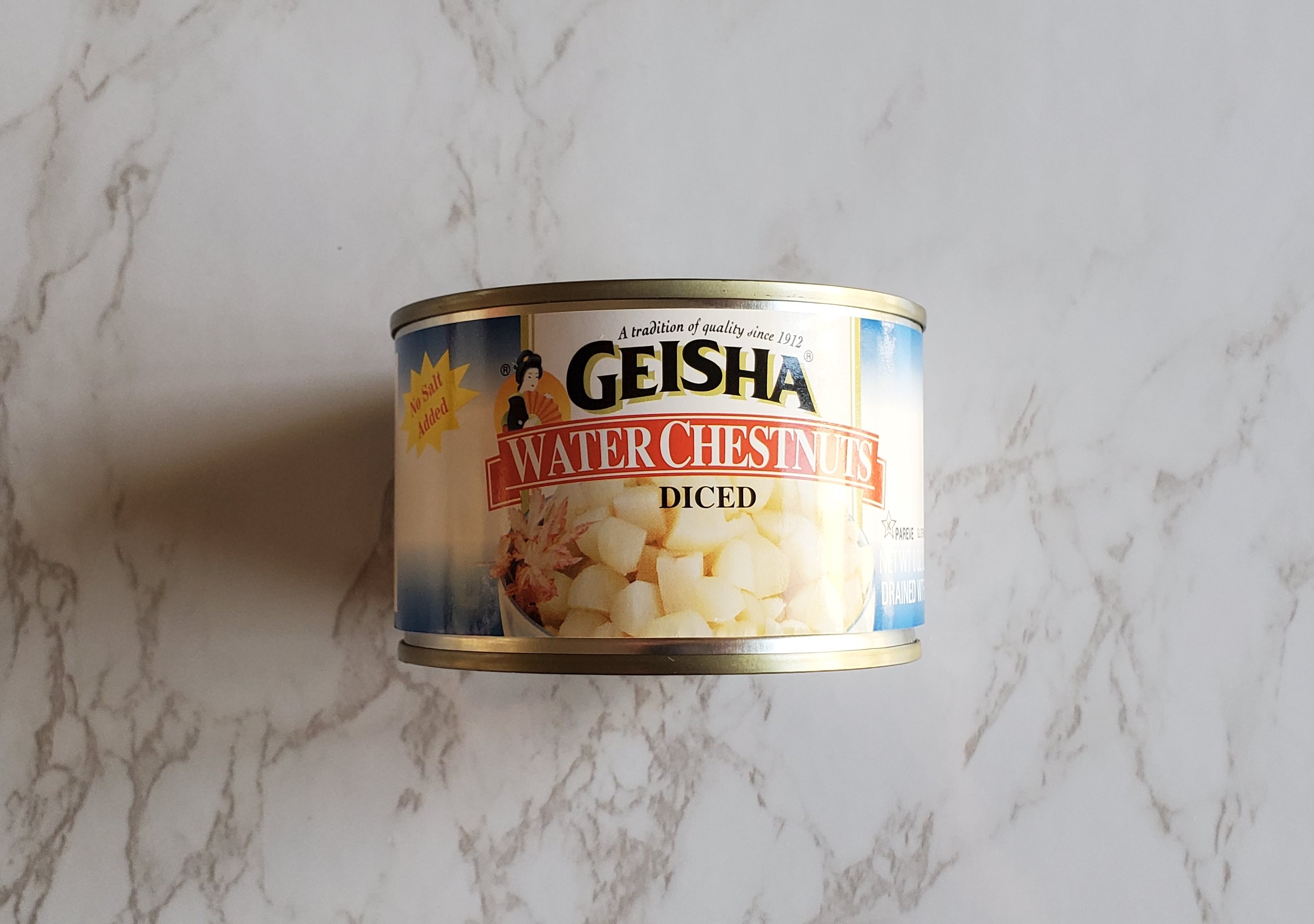 A small can of Geisha's diced water chestnuts sits on a white marbled backdrop. 