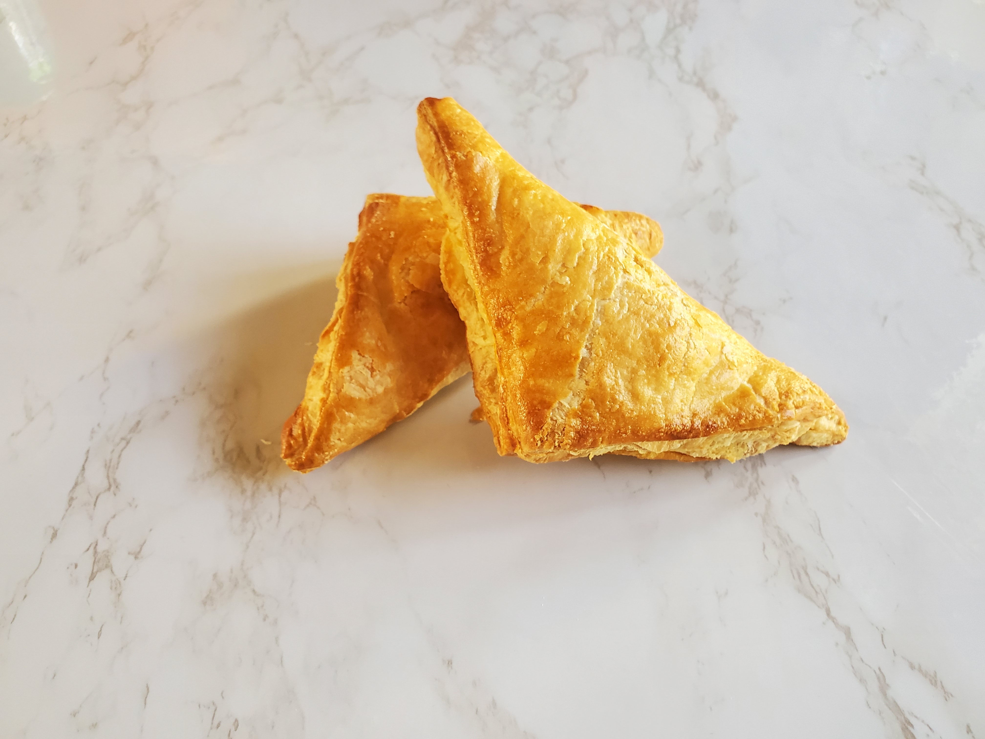 Two triangular beef curry puffs stacked on top of each other on a white marble countertop.