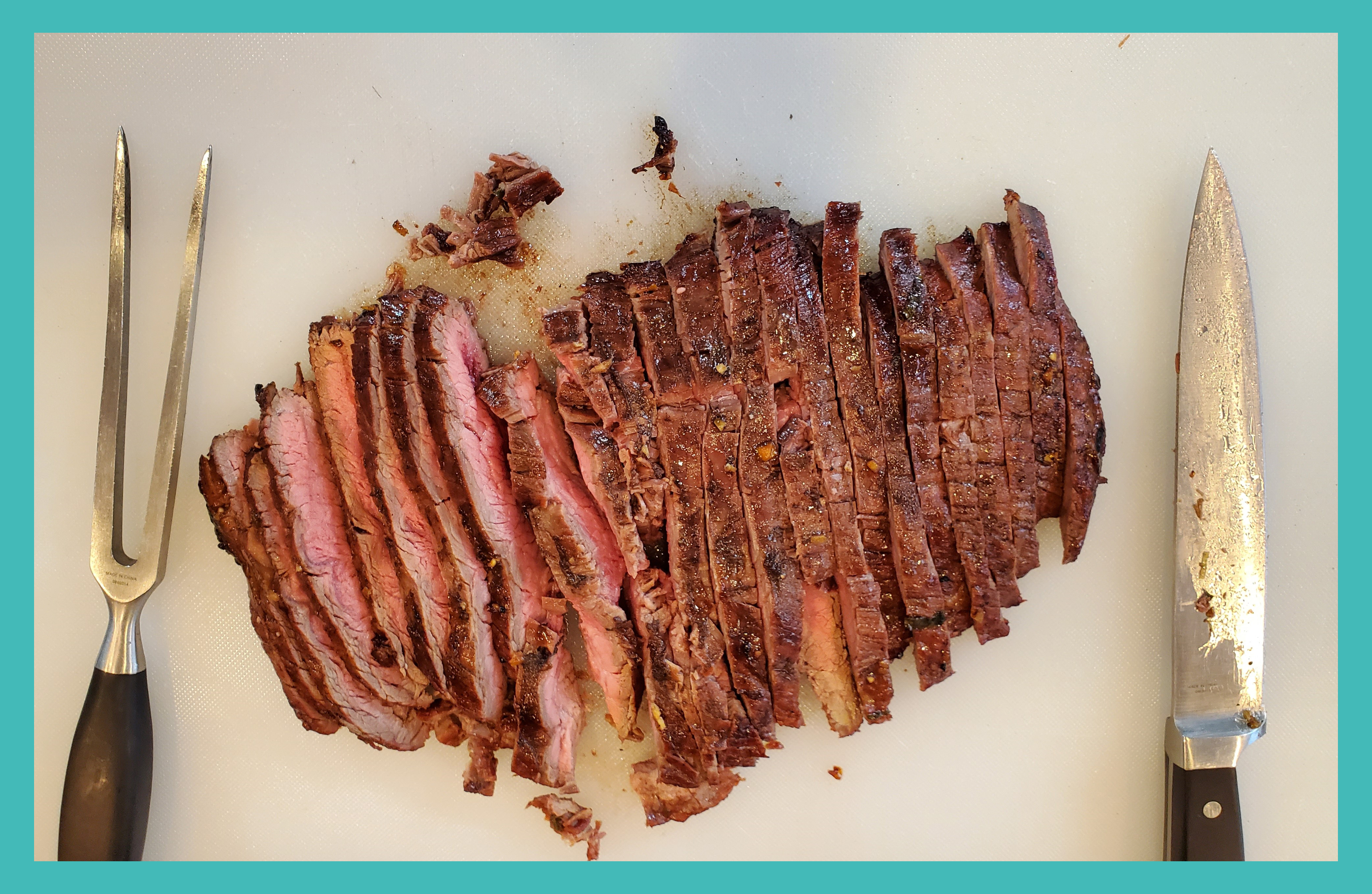 Sliced up flank steak on a cutting board with a knife and meat two pronged fork.