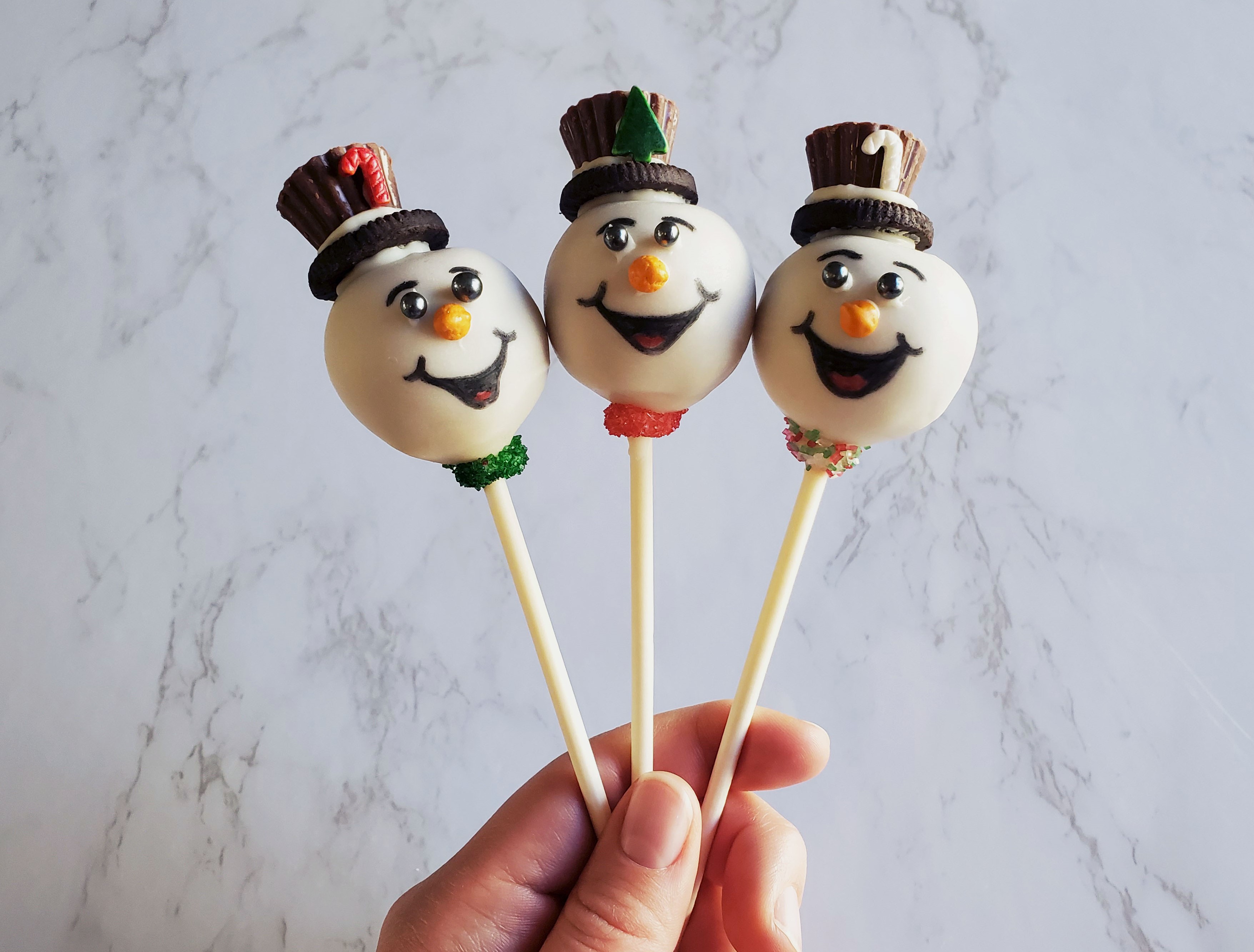 Three snowman cake pops with Reese's/oreo top hats and faces draw on with food markers.