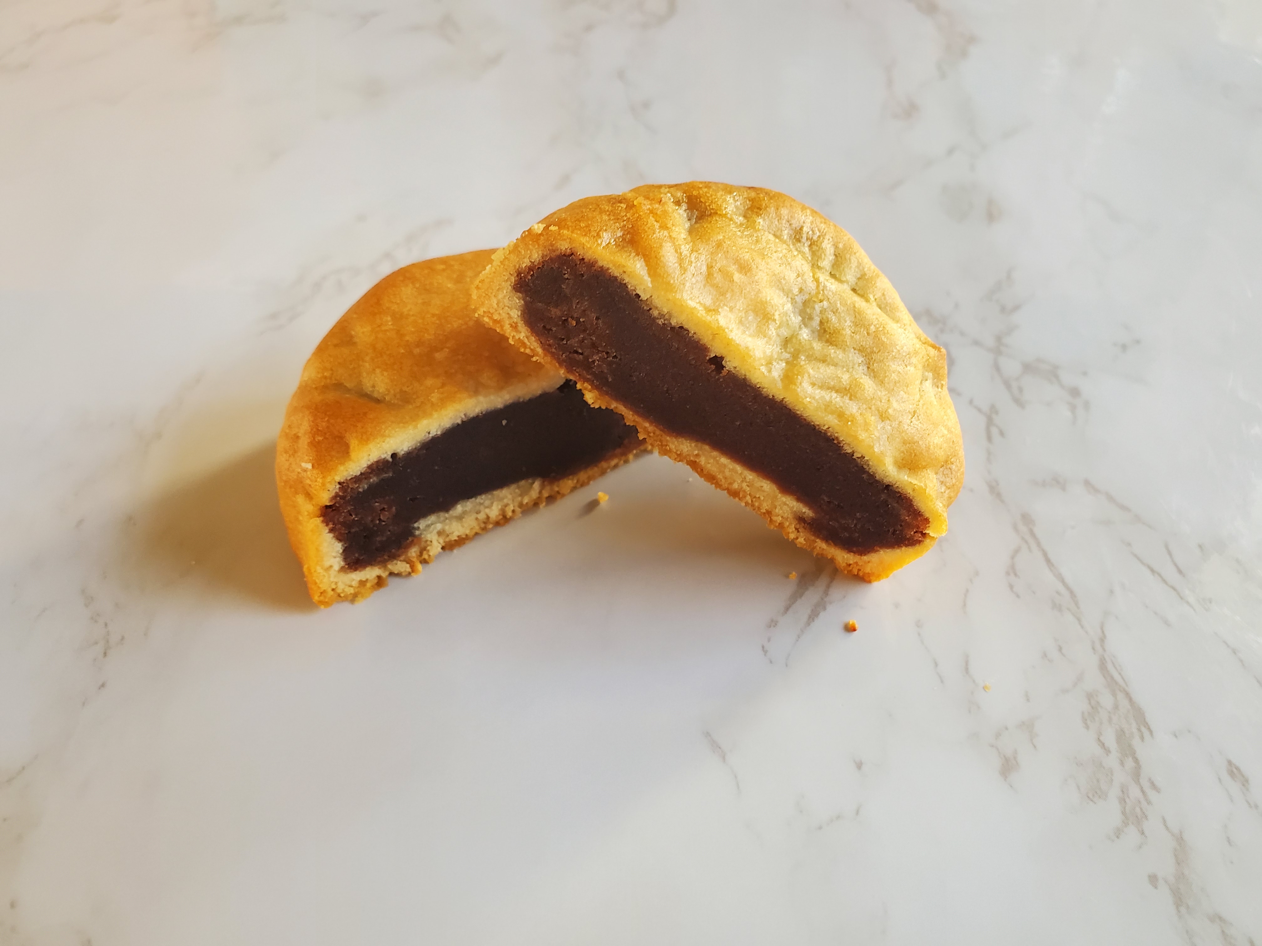A red bean mini mooncake cut in half on a white marble countertop.